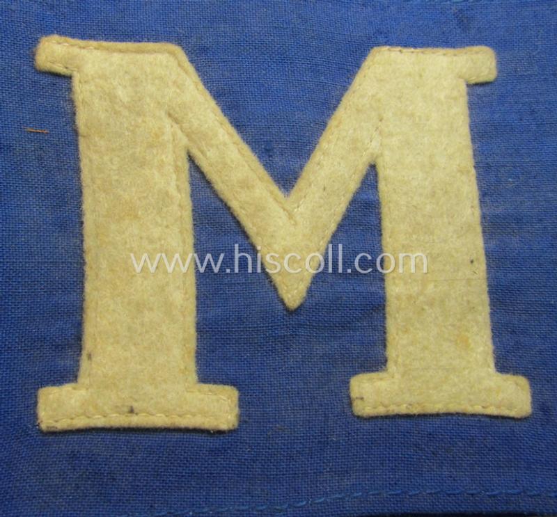 Neat, linnen-based- and/or blue-coloured armband (ie. 'Armbinde') depicting a felt-woolen-based, capital 'M'-character as was presumably intended for staff-members (ie. 'Melder') of the German RLB (ie. 'Reichsluftschutz-Bund')