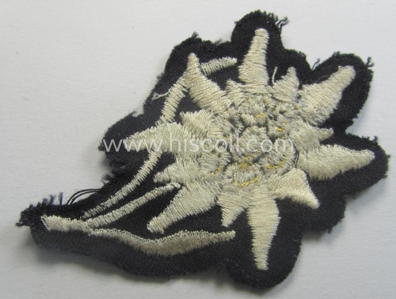 Waffen-SS-pattern, black-coloured M43-cap-insignia (ie. 'Mützenabzeichen') depicting an: 'Edelweiss'-flower as used by the various 'Gebirgsjäger'- (ie. mountain-troops-) related divisional-staff
