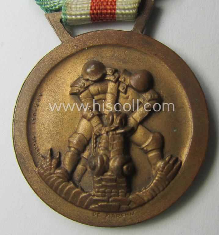 Golden-bronze-coloured- (and I deem 'Buntmetall'-based-) example of a: 'Deutsch-Italienische Feldzugsmedaille' (or: German-Italian campaign-medal) that comes mounted onto its (regular-sized) piece of original (and minimally faded!) ribbon