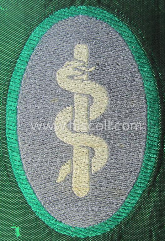 Attractive, 'Sicherheits- u. Hilfsdienst' (ie. 'SHD'-) armbadge (ie. 'Ärmelabzeichen') being a greyish-coloured example depicting an: 'Aesculapus'-symbol as was intended for a member serving as a: 'Feldscher'