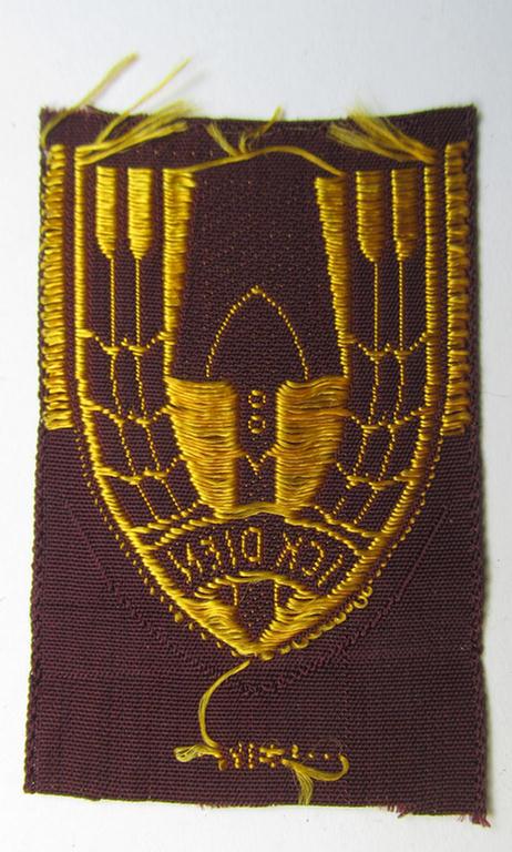 Neat - and nicely 'BeVo-woven'-like - Dutch WWII-period, labour service ie. 'Nederlandse Arbeidsdienst' (or: NAD) cap-badge entitled: 'Ick Dien' and that comes in a 'virtually mint- ie. unissued', condition
