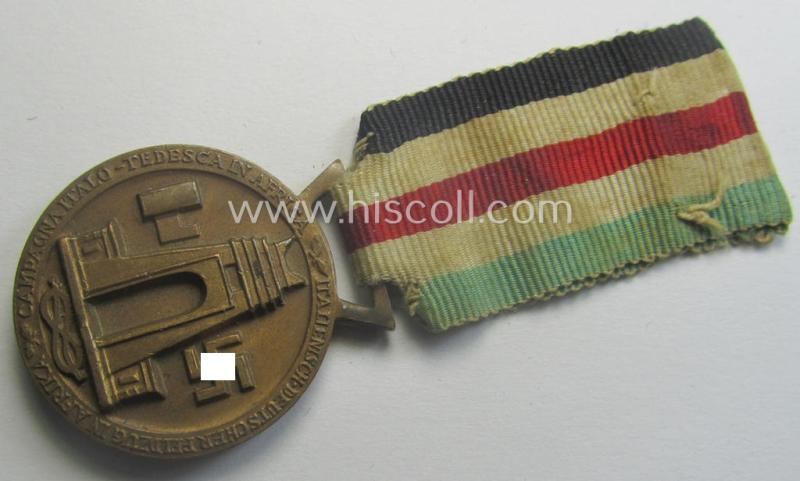 Golden-bronze-coloured- (and I deem 'Buntmetall'-based-) example of a: 'Deutsch-Italienische Feldzugsmedaille' (or: German-Italian campaign-medal) that comes mounted onto its (regular-sized) piece of original (and minimally faded!) ribbon