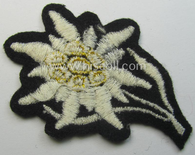 Waffen-SS-pattern, black-coloured M43-cap-insignia (ie. 'Mützenabzeichen') depicting an: 'Edelweiss'-flower as used by the various 'Gebirgsjäger'- (ie. mountain-troops-) related divisional-staff