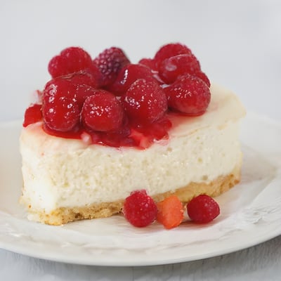 A white plate topped with a cheesecake covered in raspberries