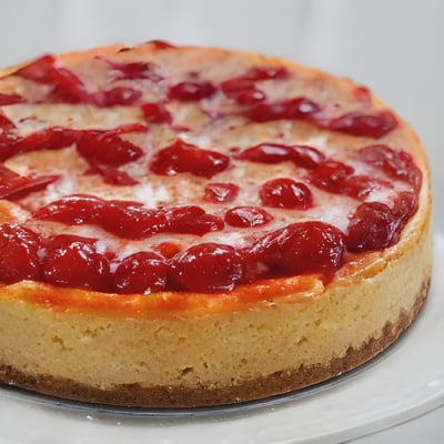 A cheesecake topped with cherries on a white plate