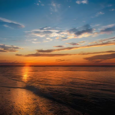 The sun is setting over the water on the beach