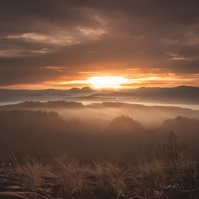 The sun is setting over the mountains in the fog