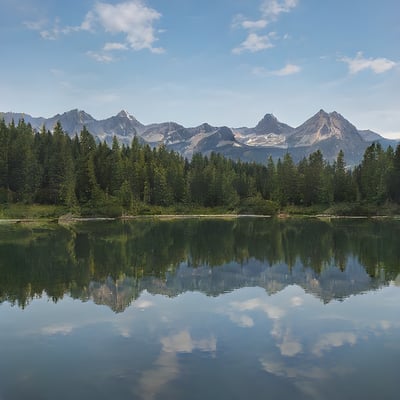 A lake surrounded by trees and mountains under a blue sky