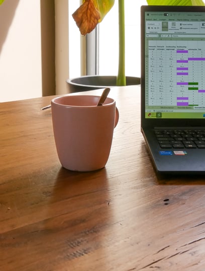 laptop met excel overzicht en roze kopje op houten tafel
