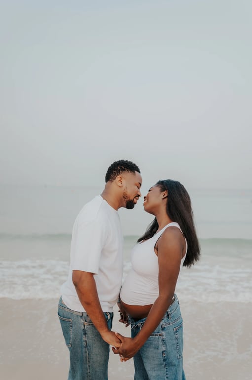 Expecting couple facing one another and holding hands beside the sea.