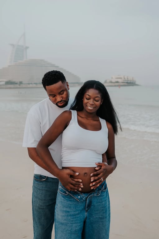 Expecting couple holding her bump together, with the sea and Burj Al Arab behind them.