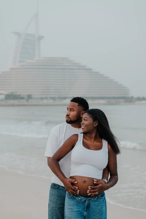 Expecting couple holding her bump together, with the sea and Burj Al Arab behind them.