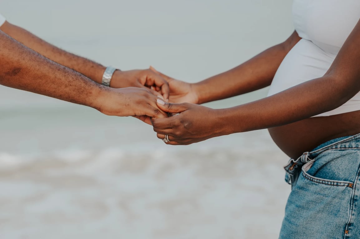 Close-up of the couple’s joined hands beside her bump and blue jeans.