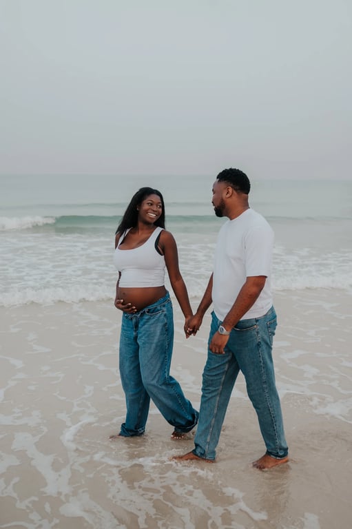 Expecting couple holding hands barefoot in the shallow surf during their beach maternity photoshoot.