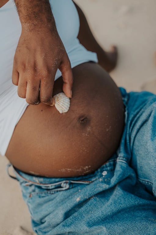 Close-up of a small white shell held against a pregnant woman’s bump above her blue jeans.
