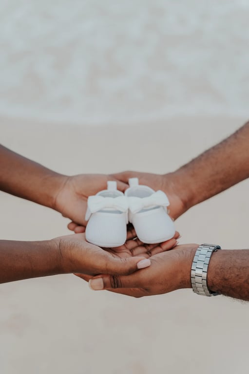Close-up of the couple’s hands holding a pair of tiny white baby shoes beside the sea.