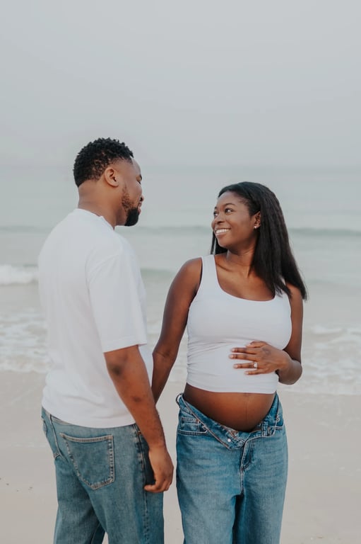 Pregnant woman smiling at her partner as they stand together at the beach.