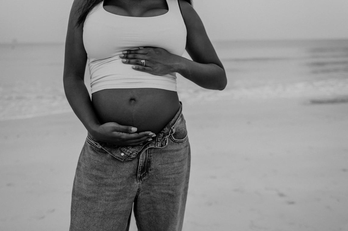 Black and white detail of a pregnant woman’s hands resting above and below her bump, with blue jeans and a white top.