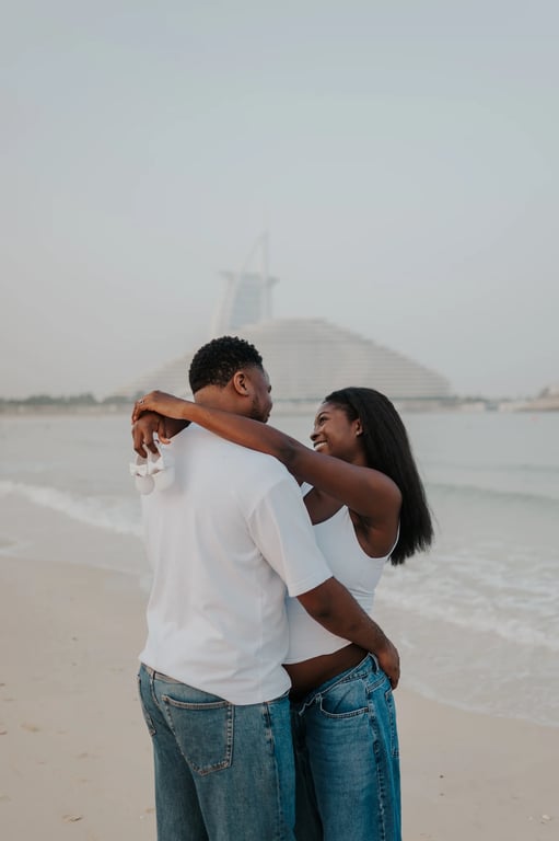 Expecting couple facing and embracing one another on the beach, with Burj Al Arab in the distance.