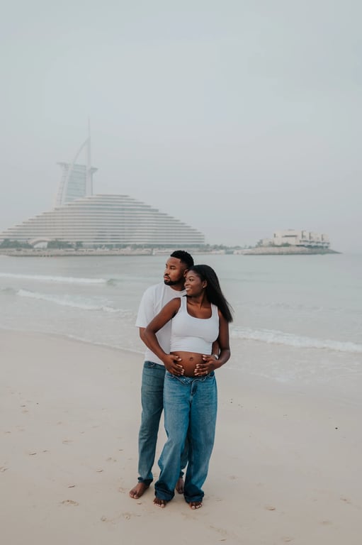 Expecting couple holding her bump together, with the sea and Burj Al Arab behind them.
