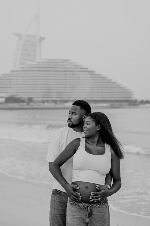Black and white expecting couple holding her bump together, with the sea and Burj Al Arab behind them.