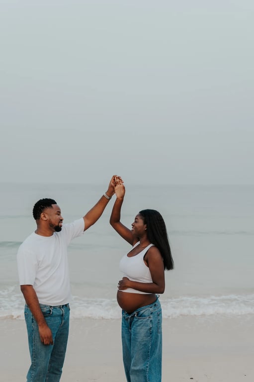 Expecting couple lifting their joined hands on the sand beside the sea.