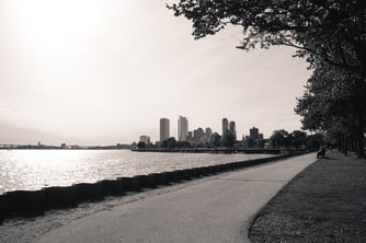  Black and white view of a lakeside path with city skyline in the background.