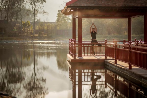 Qigong vs Yoga - a woman practicing yoga in a gazebo by the water 