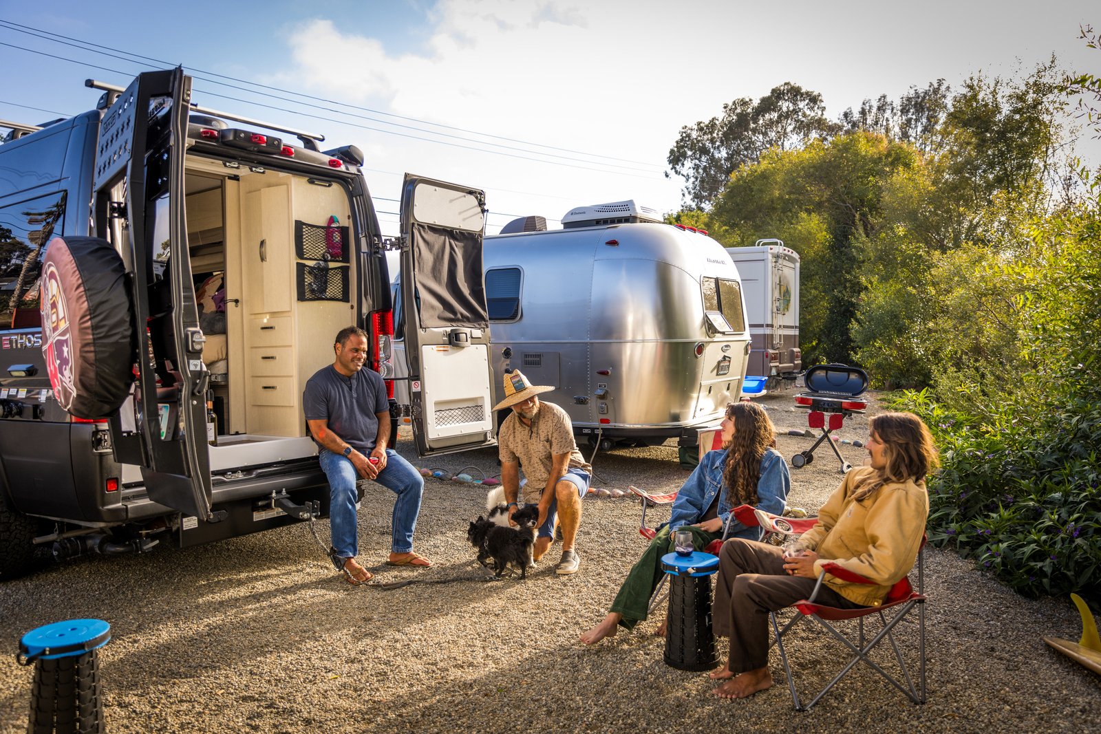 Four people and dogs beside an open campervan and an Airstream at Beach RV Pleasure Point.