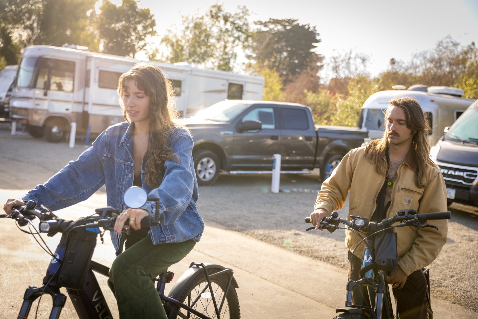 Two people on electric bicycles with parked RVs behind them at Beach RV Pleasure Point.