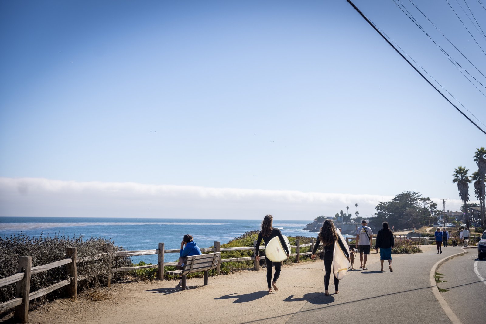 People carrying surfboards and walking along the oceanfront path at Pleasure Point.