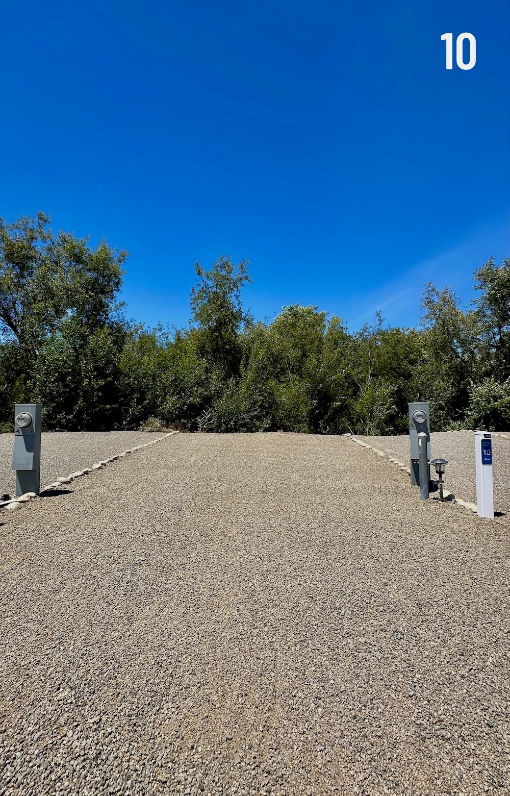 Empty Standard Plus site 10, a wider creekside gravel pad with full hookups