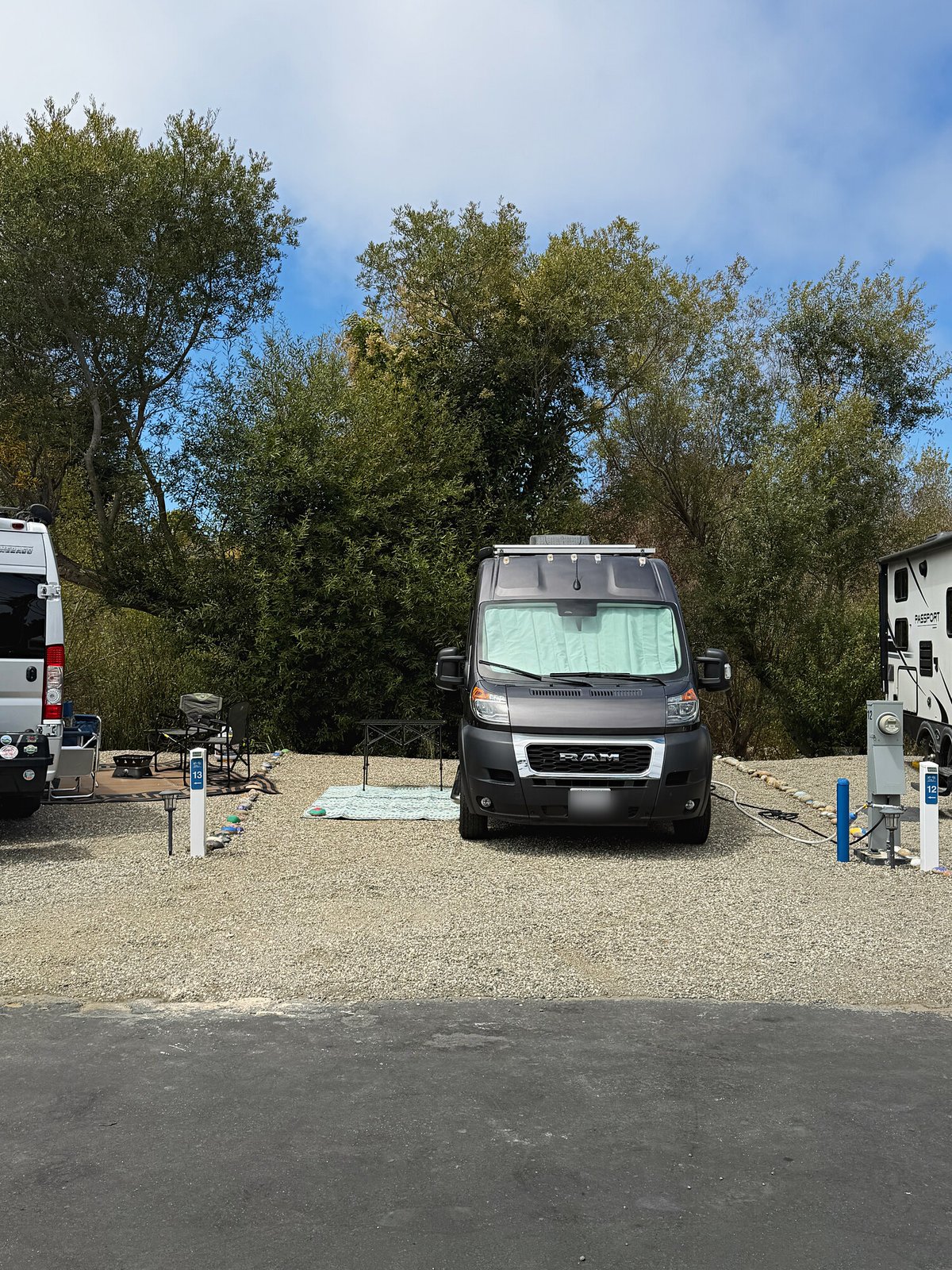 Camper van backed into a Standard gravel site beneath the trees