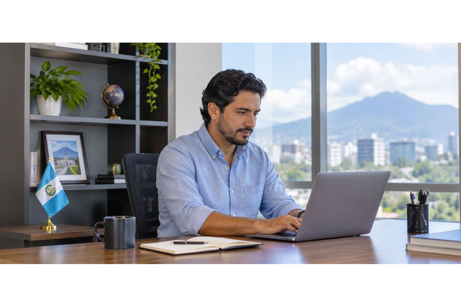 Homme travaillant sur un ordinateur portable à un bureau, avec un petit drapeau guatémaltèque à proximité.