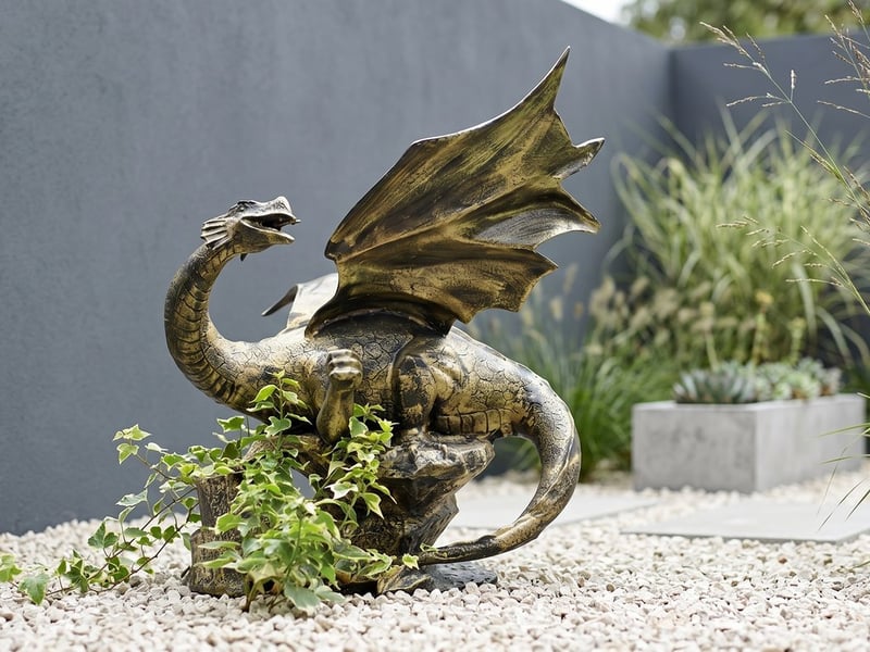 Aged bronze winged metal dragon garden ornament rearing up on pale gravel against an anthracite grey wall in a modern courtyard garden