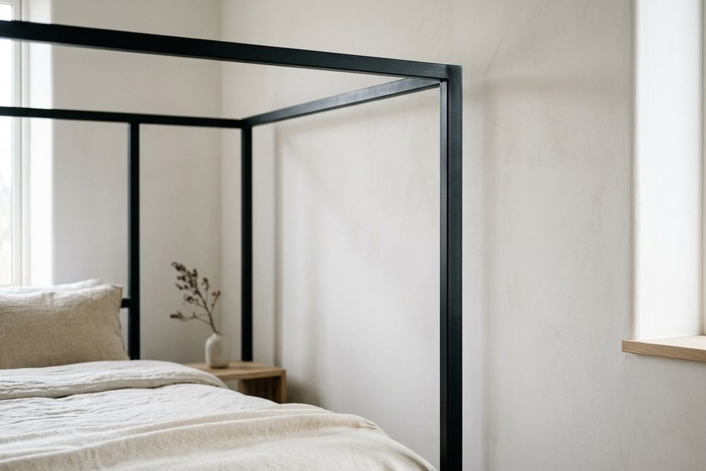 Close-up of a slim black metal four-poster frame against a pale wall
