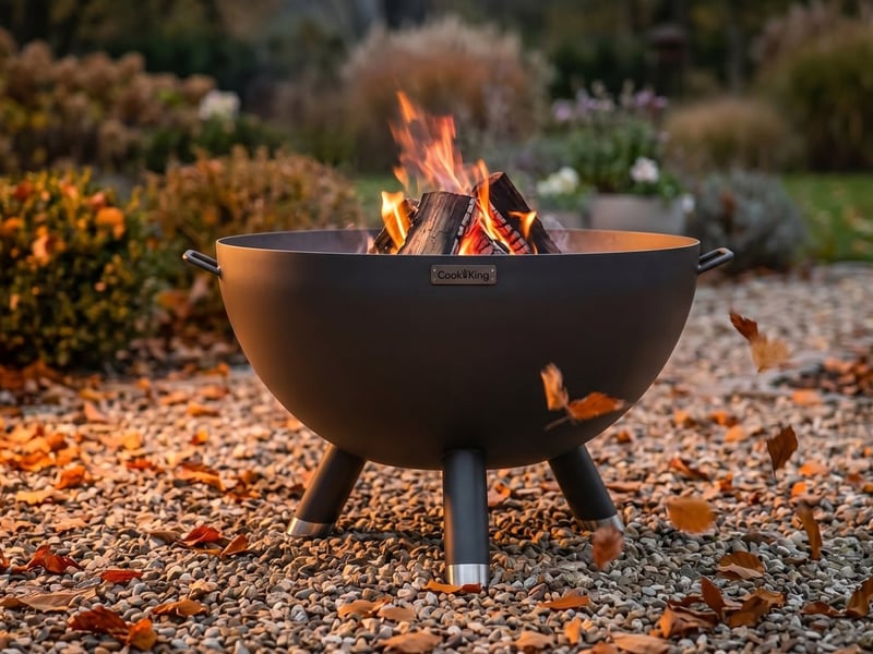 Deep steel Cook King Kongo fire bowl lit on a gravel area on a breezy autumn evening with fallen leaves around