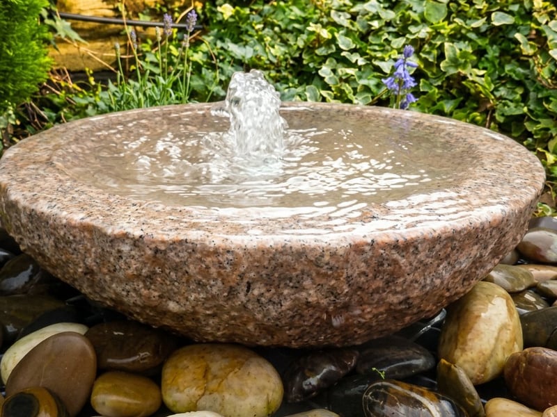 Babbling Bowl Pink Granite water feature with a single bubbling spout set in a UK pebble bed