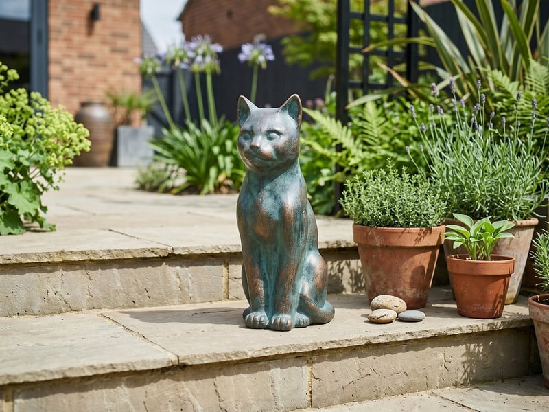 Cast iron sitting cat garden ornament in verde bronze on stone patio steps beside terracotta pots