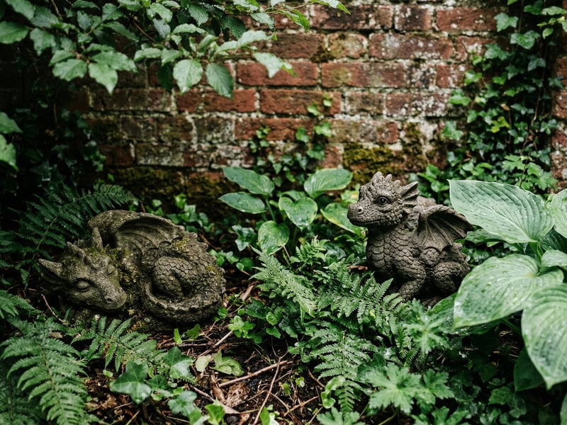Stone dragon hatchling garden ornaments nestled among ferns in a shaded UK garden border