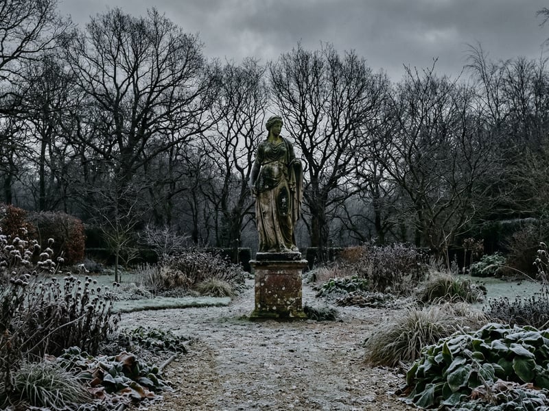 A large stone garden statue as a focal point in a winter garden with bare branches and frost