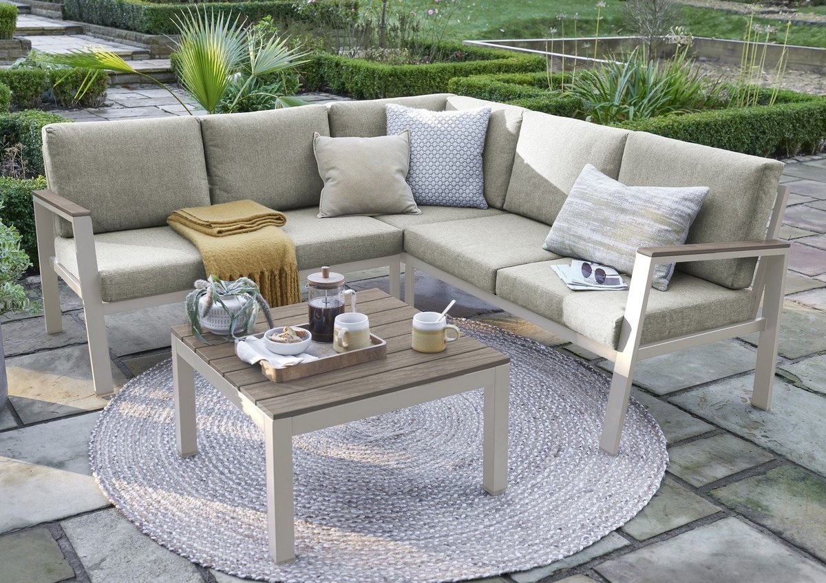 Beige aluminium mini corner sofa set with taupe cushions and round rug on sandstone paving framed by box hedging in a small UK patio garden