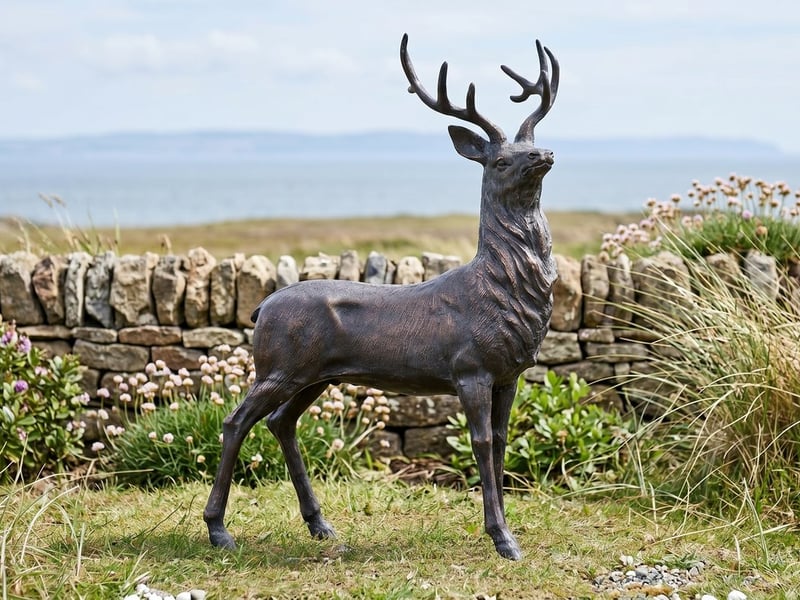 Bronze maned stag garden ornament on coastal turf above the sea in a UK seaside garden with marram grass