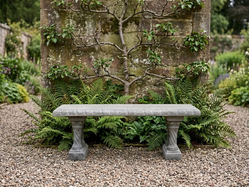 Straight Pattern stone garden bench on gravel in a walled garden with an espaliered fruit tree behind