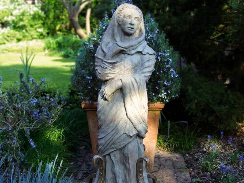 Draped Maiden cast stone garden statue secured on a level paving slab base in an English garden