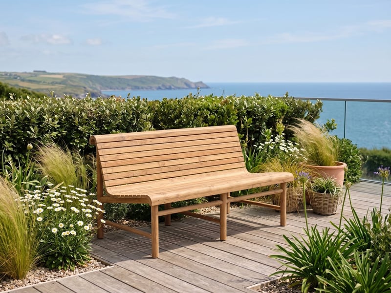 Station double teak garden bench on decking overlooking the sea in a coastal Devon garden