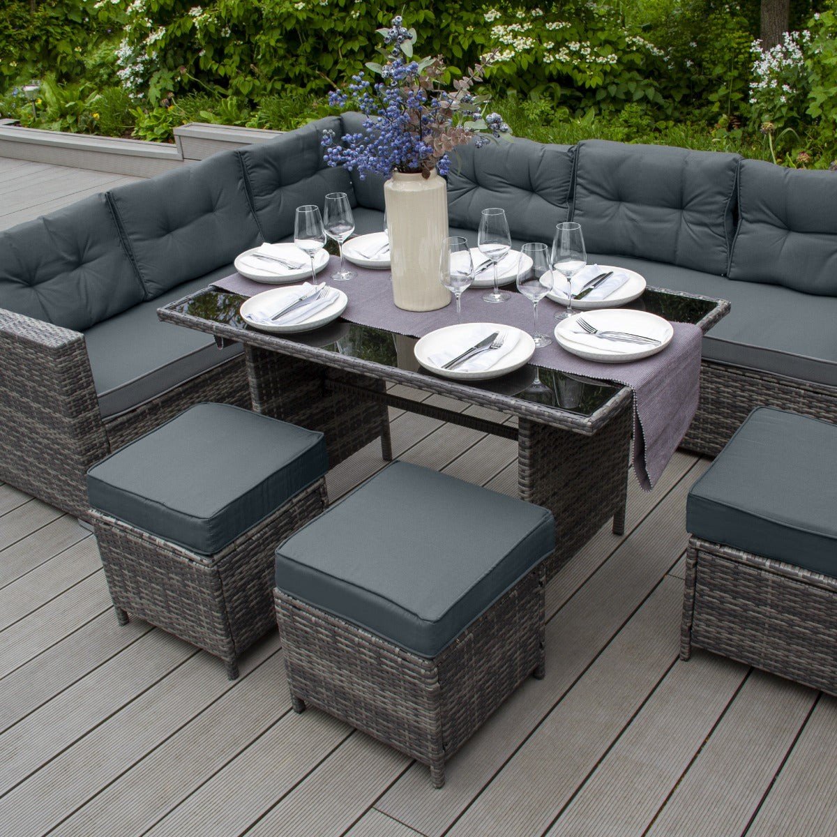 Grey rattan U-shaped 9 seater garden corner sofa set with dining table and stools on composite decking in a square UK garden