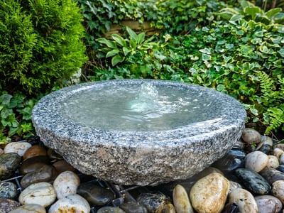 Grey granite babbling bowl water feature on pebbles, a pondless alternative to a patio pond