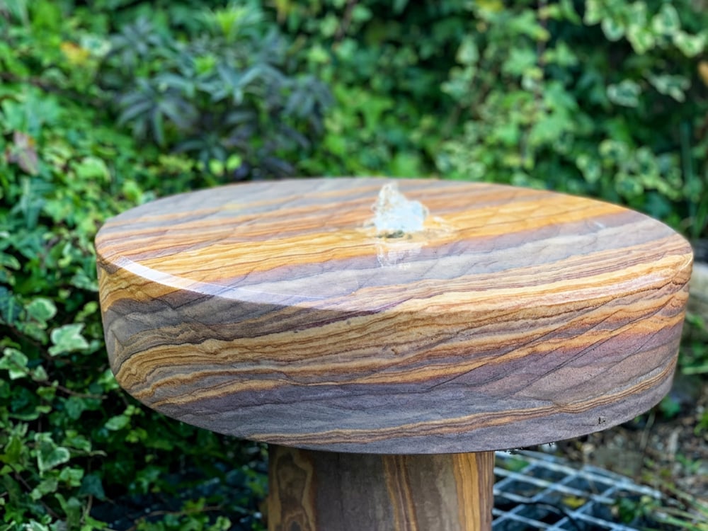 Rainbow sandstone millstone water feature on its reservoir grid, a porous stone that needs draining for winter