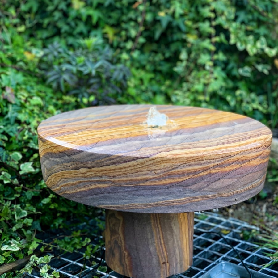 Rainbow sandstone millstone water feature in a UK Japanese stroll garden with raked gravel and granite lantern